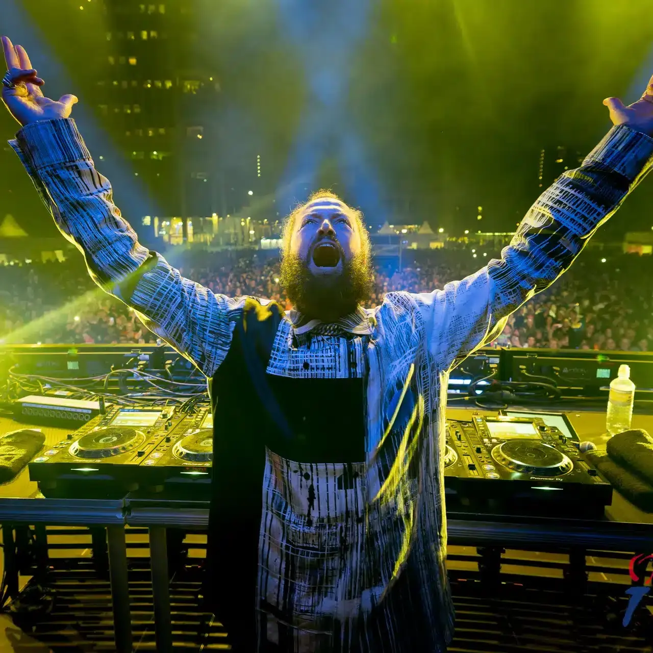 DJ op festivalstage met publiek onder geel-blauwe lichten en stadsachtergrond
