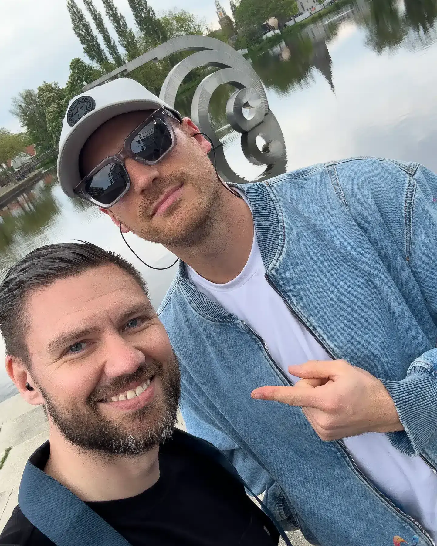 Selfie van twee mannen bij kalm water en moderne metalen sculptuur in Zoetermeer.