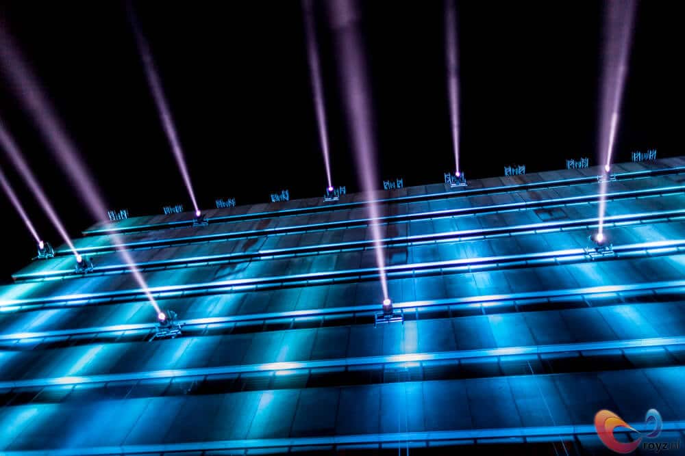 Nachtbeeld van een blauwe gevel met paarse stralen en moderne lichtshow.