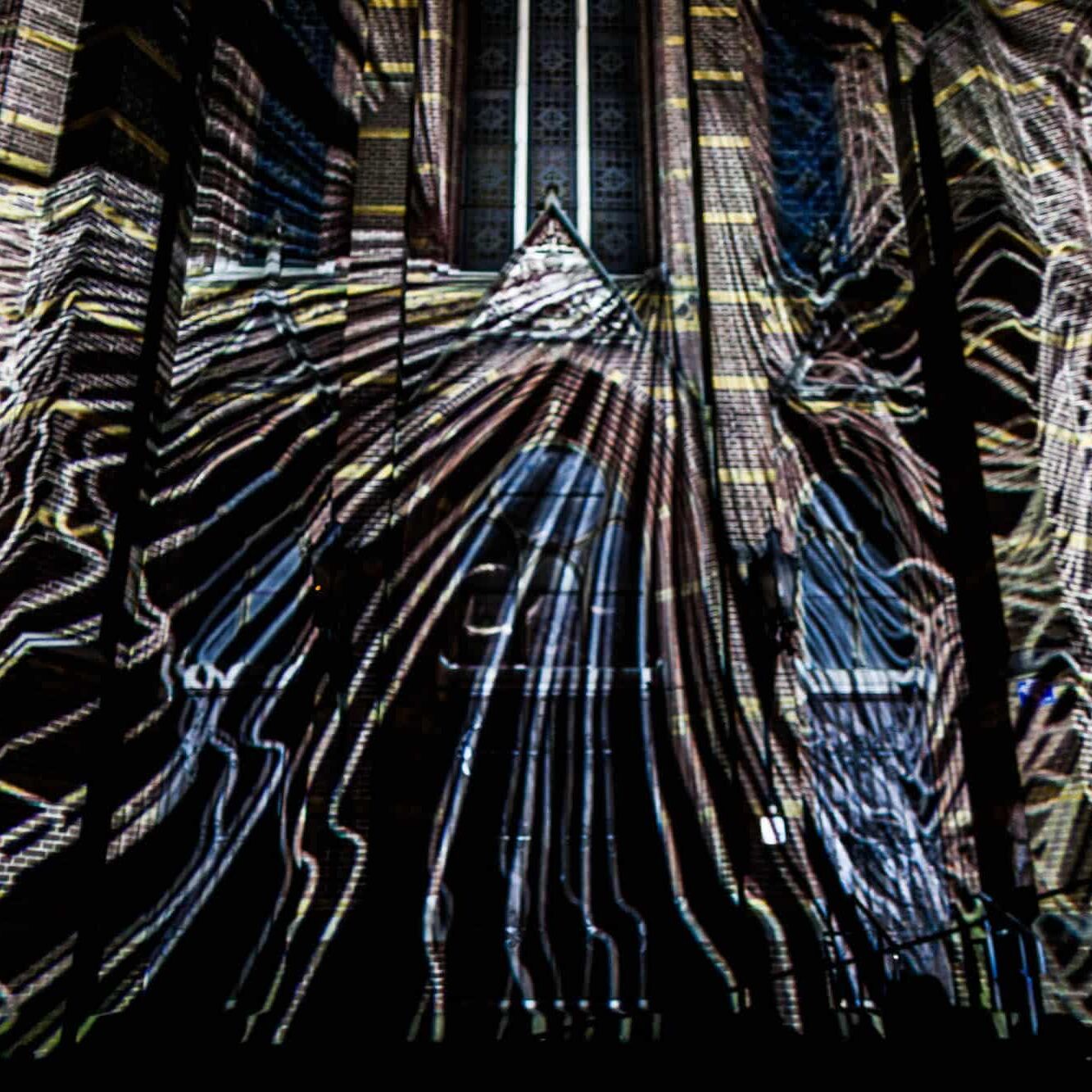 Eindhoven: gotische kathedraal bij nacht met dynamische lichtprojectie en toeschouwers.
