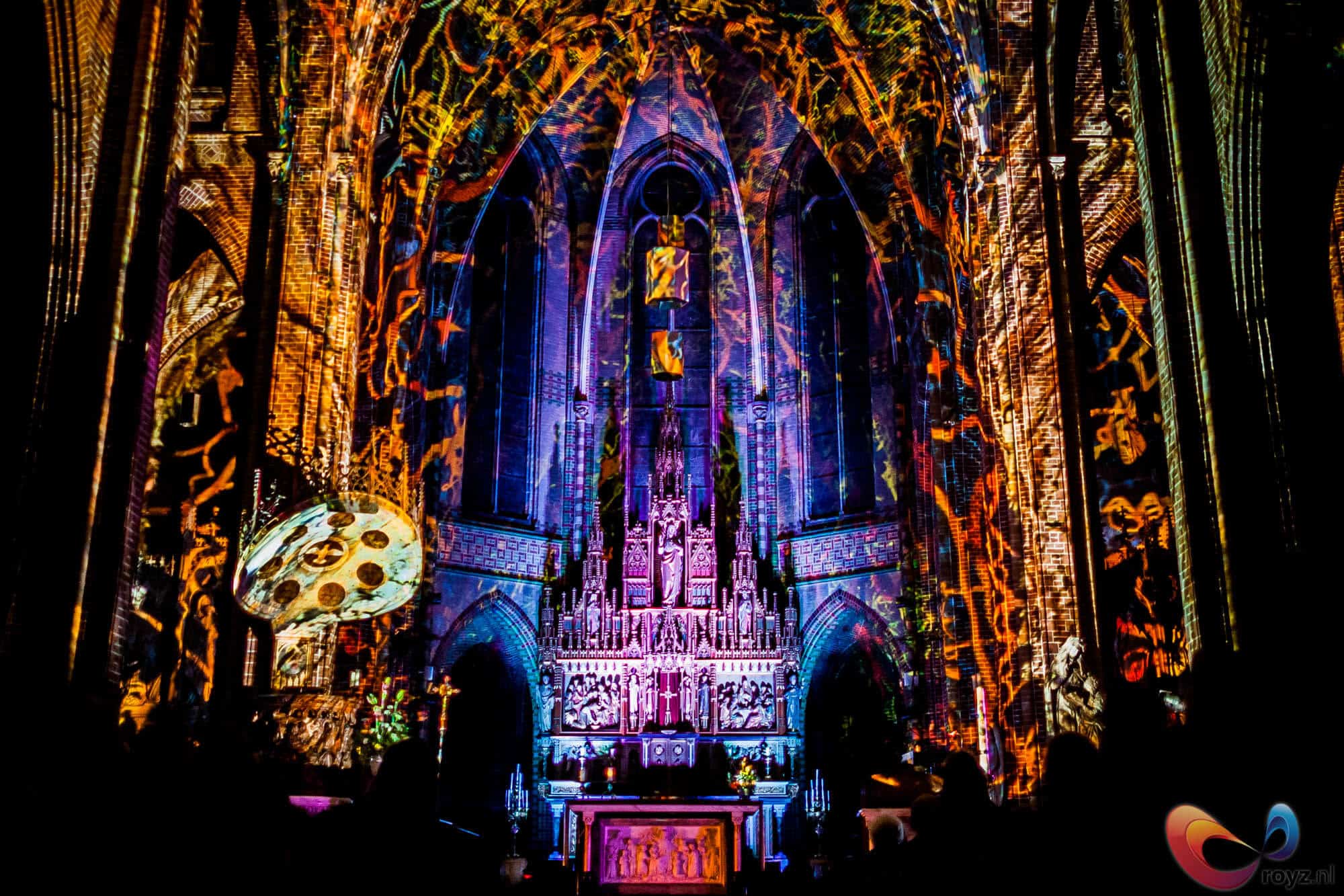 Eindhoven gotische kathedraal in lichtshow met warme amberkleur en koele blauwtinten, bezoekers als silhouetten.