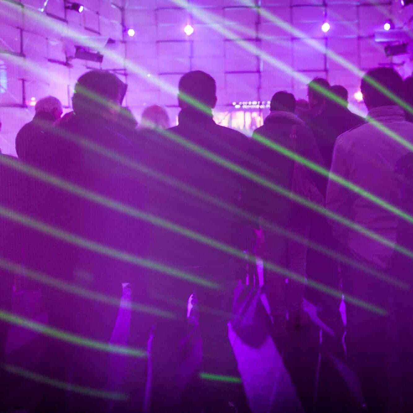 Drukke nachtclub met paars licht, groene lasers en futuristische panelen.