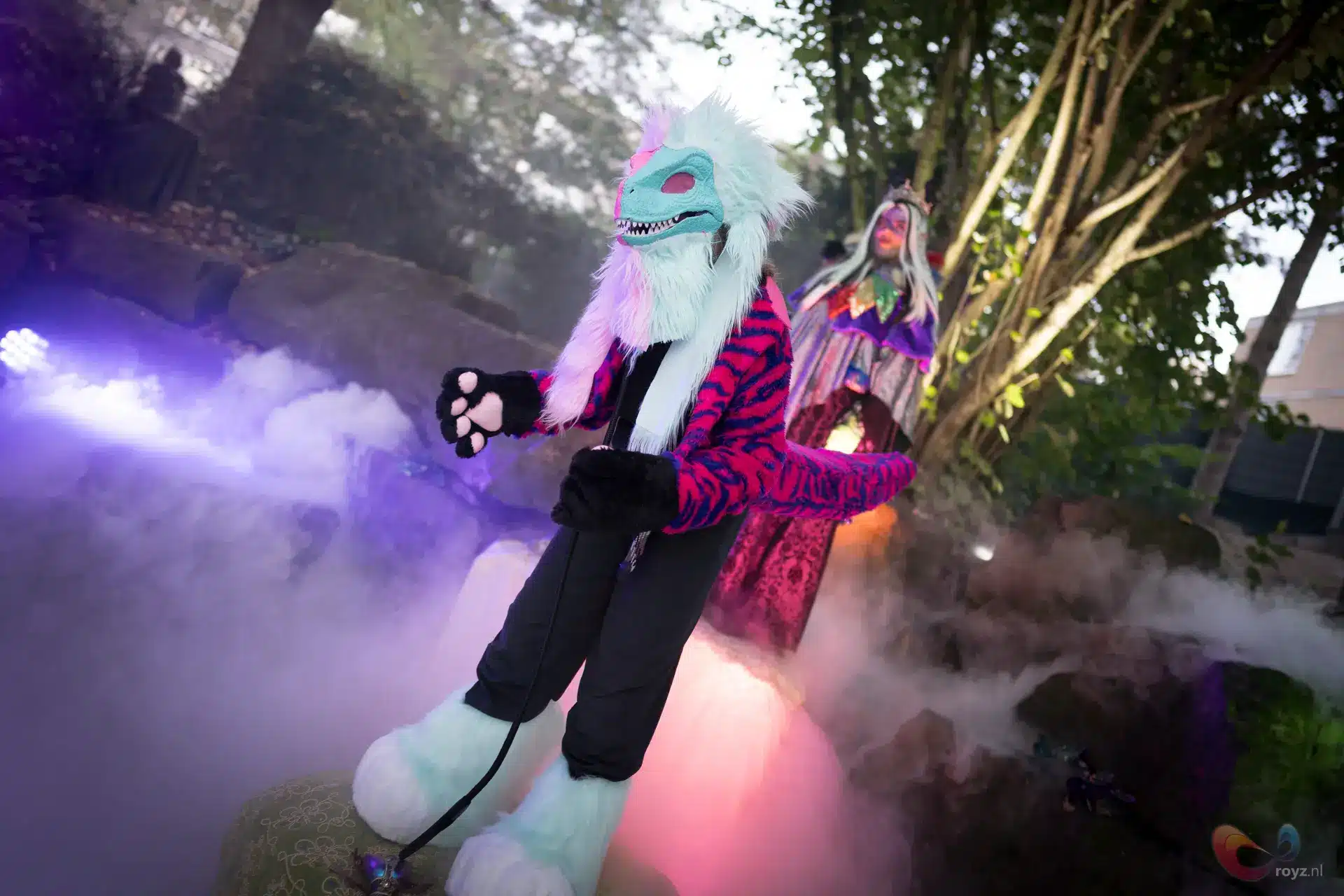 Turkoois wolfmasker en ceremoniële figuur in mistige tuin met roze en paarse verlichting.