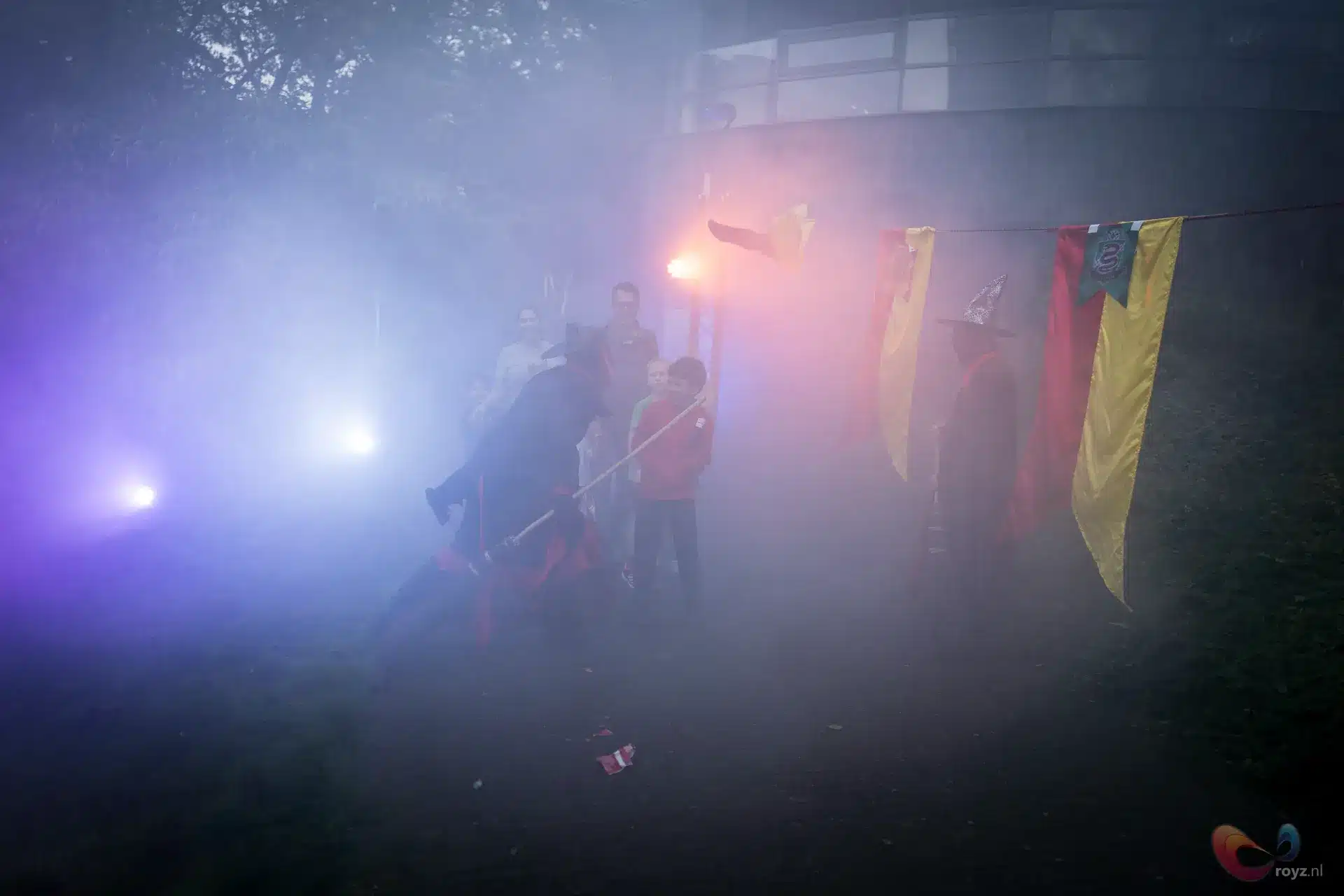 Geel en rood vlaggenlijn met fakkel in mist, silhouetten van publiek.