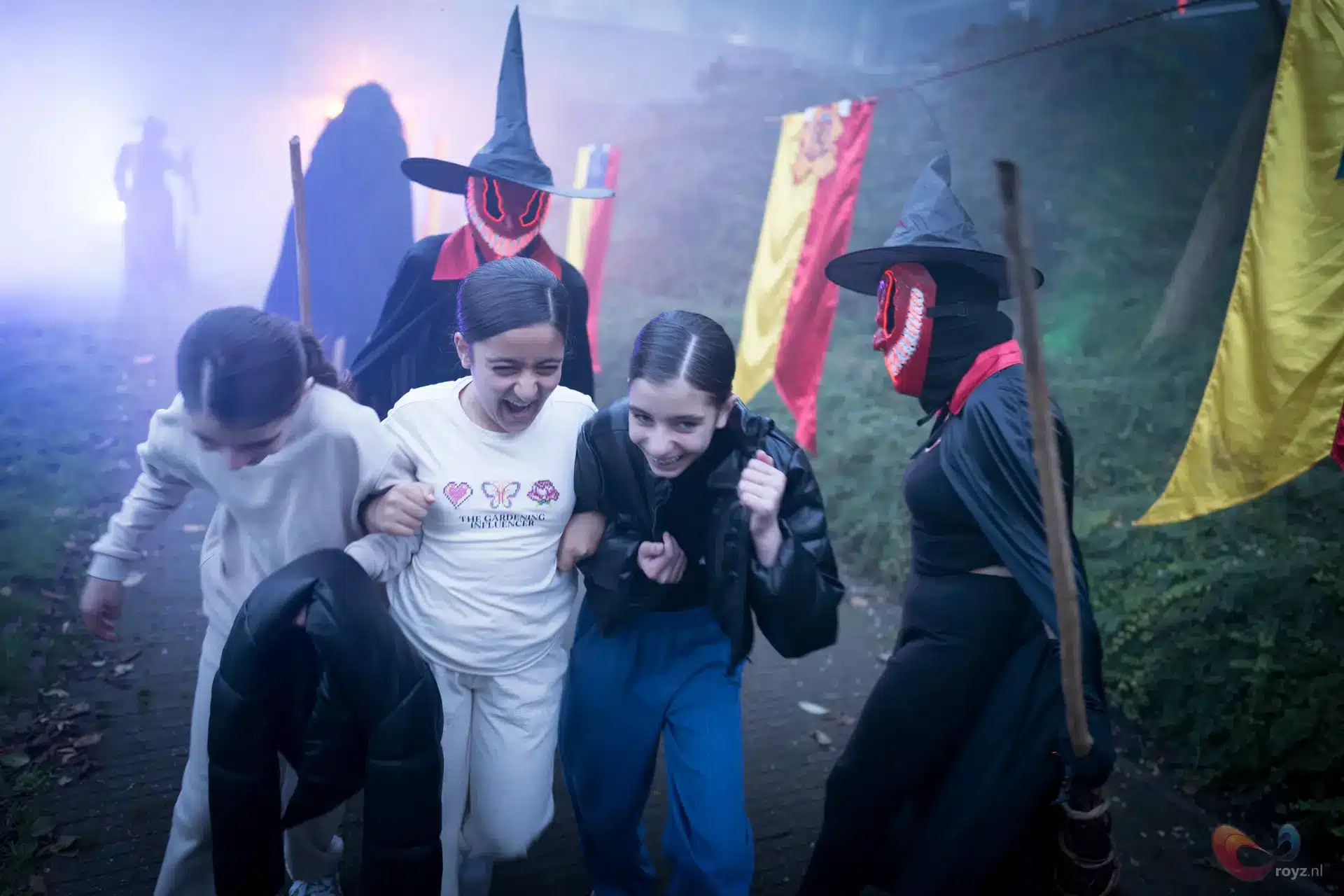 Spooktocht Zoetermeer: kinderen arm-in-arm langs kleurrijke banners, begeleid door gemaskerde spookfiguren in mist.