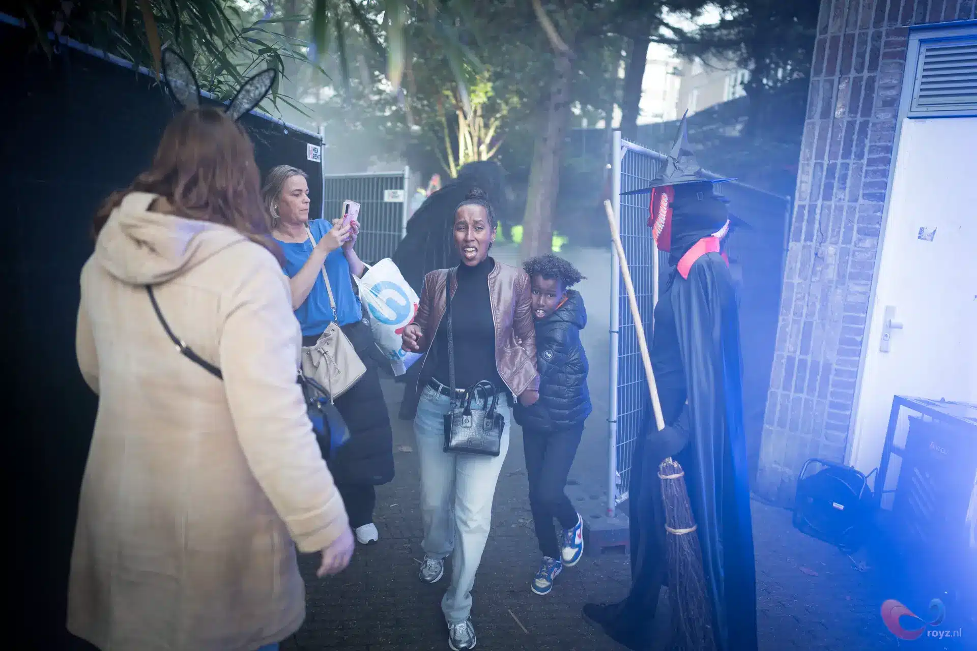 Zoetermeer Halloween: toveraar op straat in blauwe nevel; vrouw maakt foto van moeder met kind.