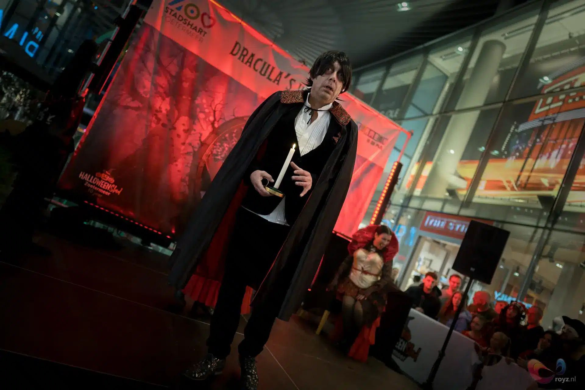 Dracula-achtige vampier op winkelcentrum podium tijdens Halloween met kaars en rode spookachtige achtergrond