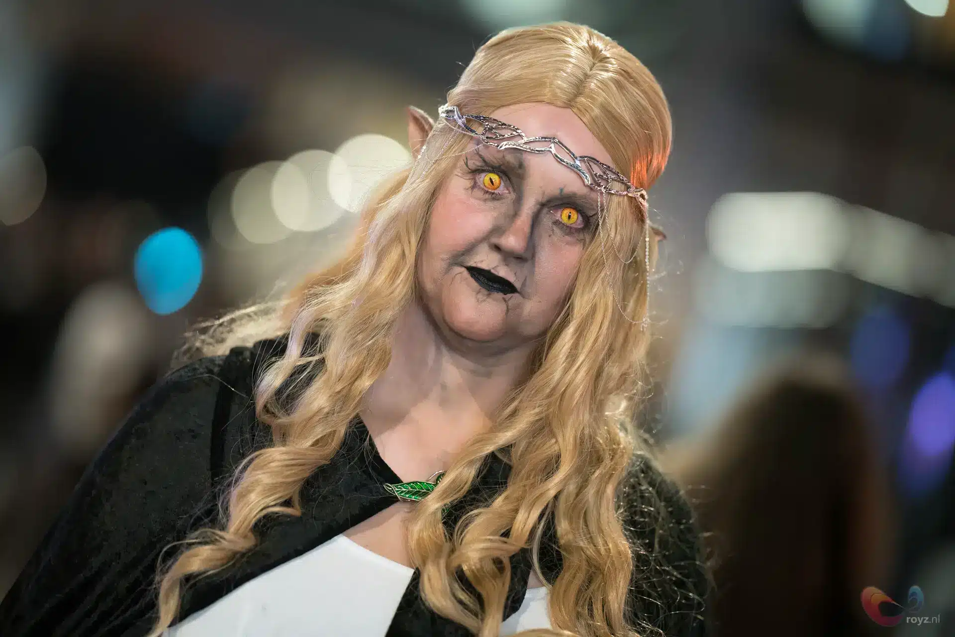 Elfachtige cosplay in gotische fantasy-stijl met bleke huid en gele katachtige ogen, zilveren voorhoofdsketting.