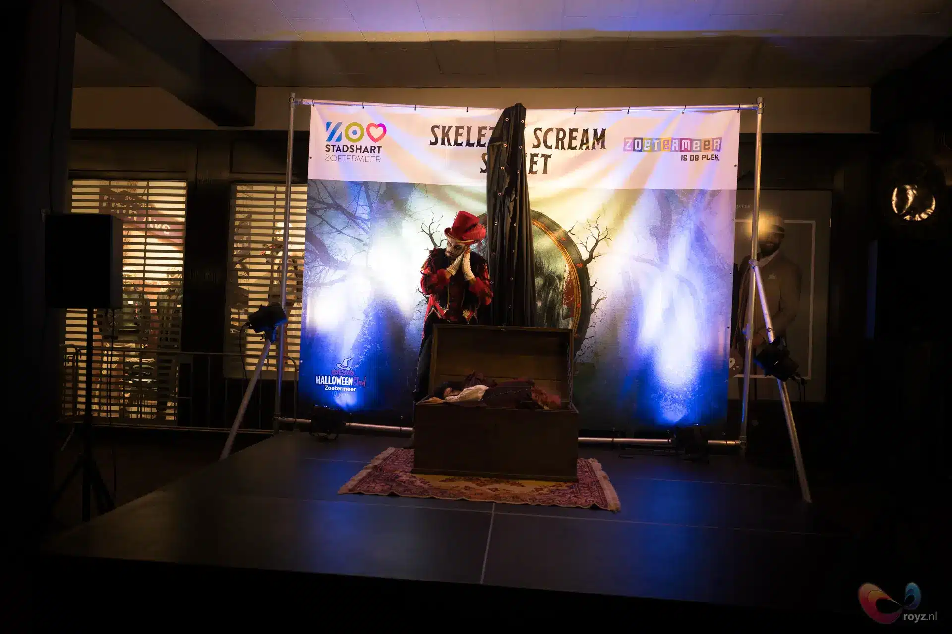 Halloween optreden met rode hoed, kist op binnenpodium, mysterieus blauw-paarse belichting.