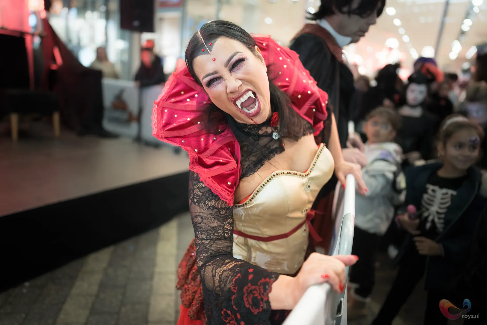 Energetische performster in gouden bustier en rode kraag op podium voor publiek.