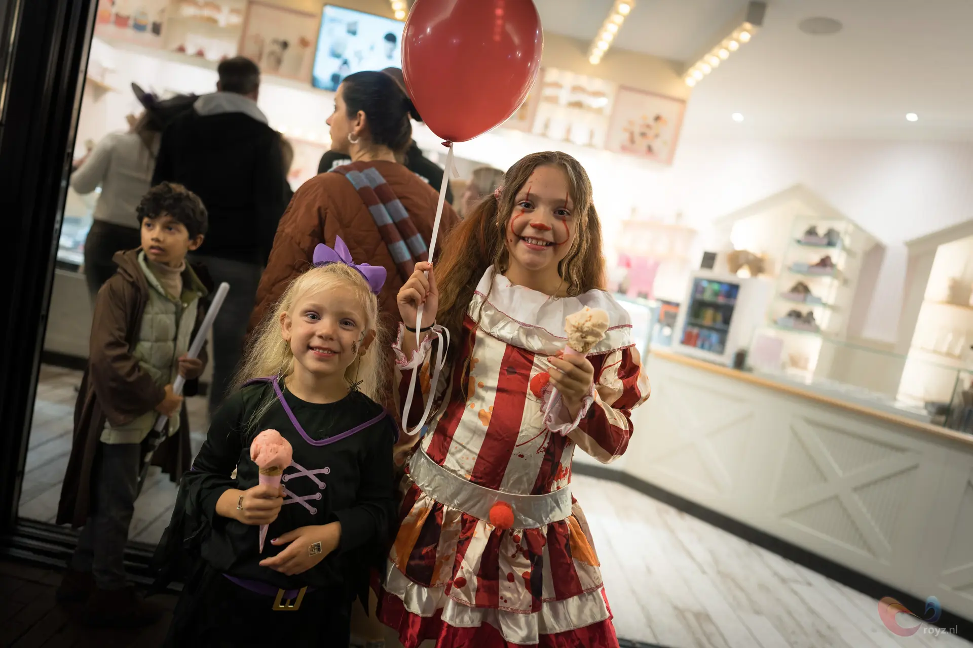 Twee meisjes in prinsessen- en circuskostuums poseren bij etalage met rode ballon.