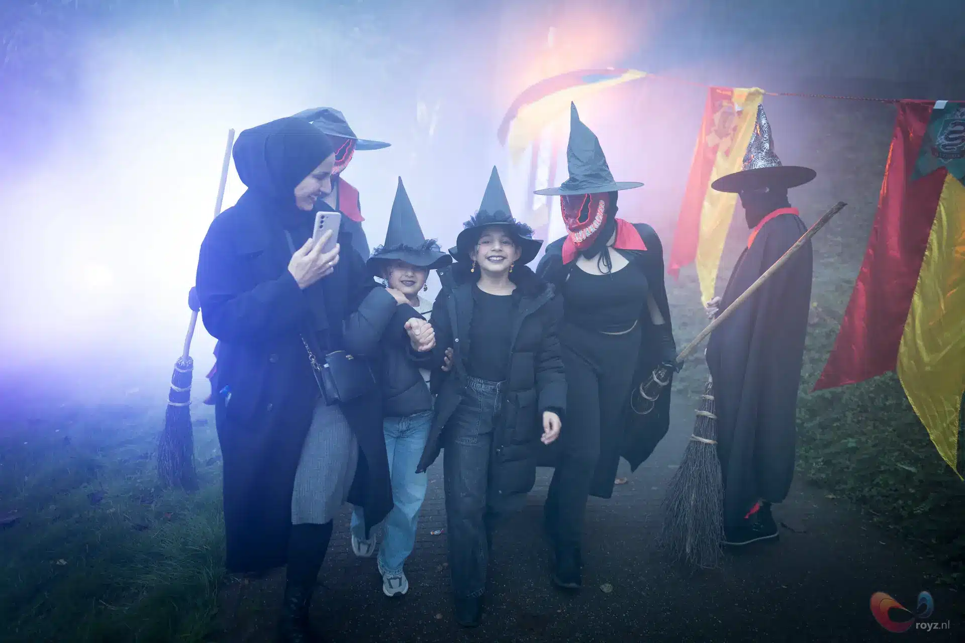 Heksenstoet op Halloween in Zoetermeer: zes mensen in kostuums langs mist en kleurrijke vlaggen.