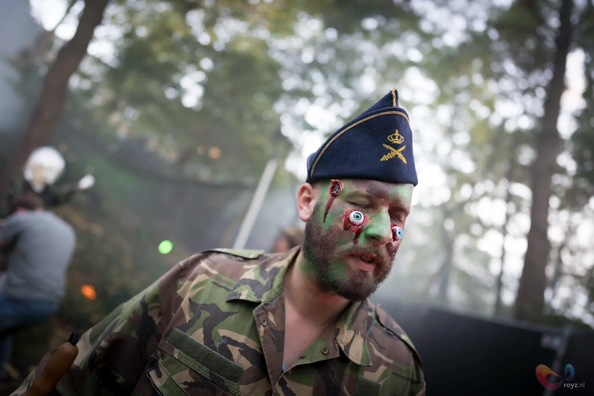 Zombie-soldaat in bos met camouflage en cartoonachtige blauwe ogen – Halloween-kostuum.