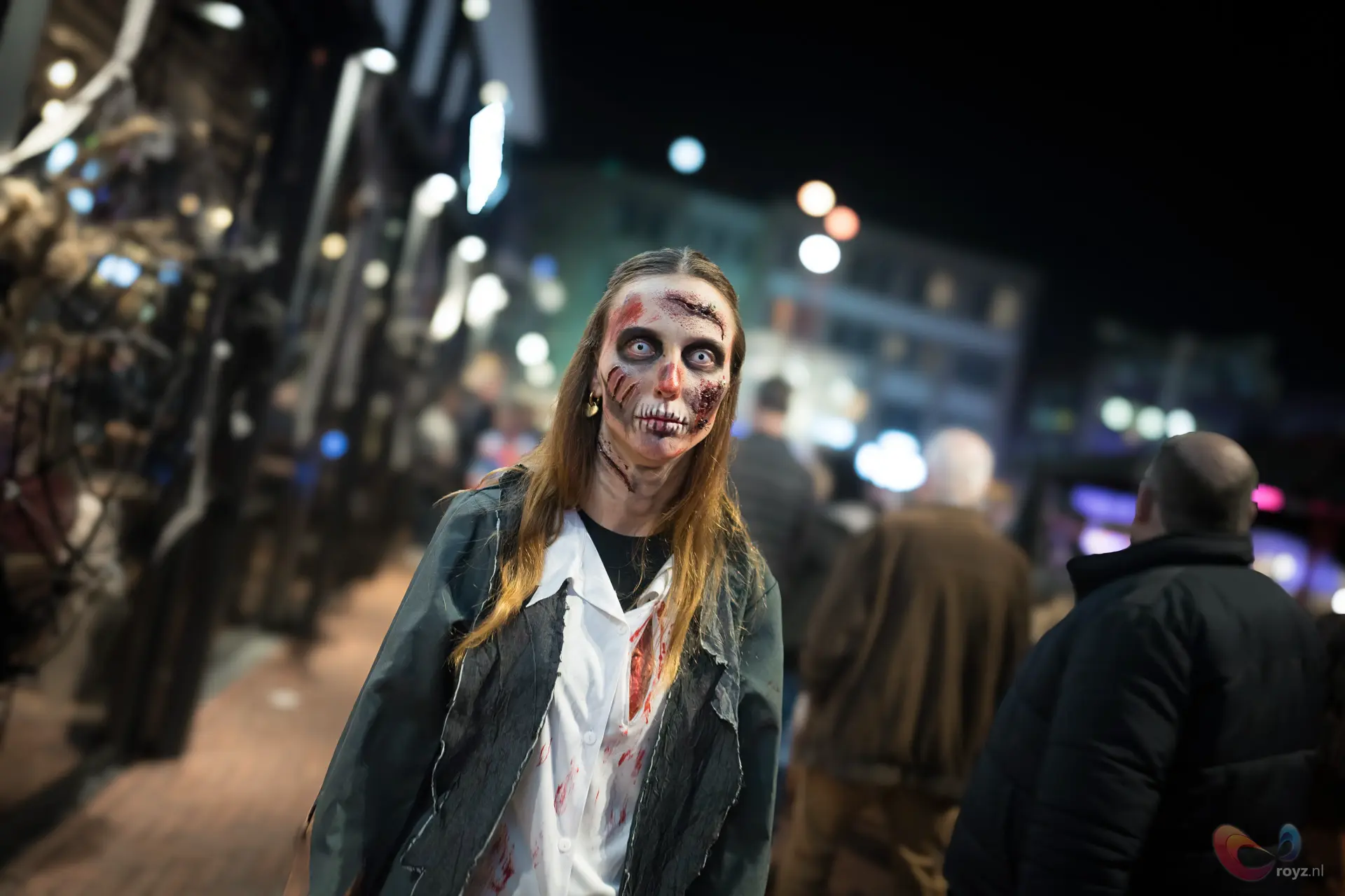 Zombie-wandelaar op Halloween in Zoetermeer met bleke huid en bokeh-lichten.