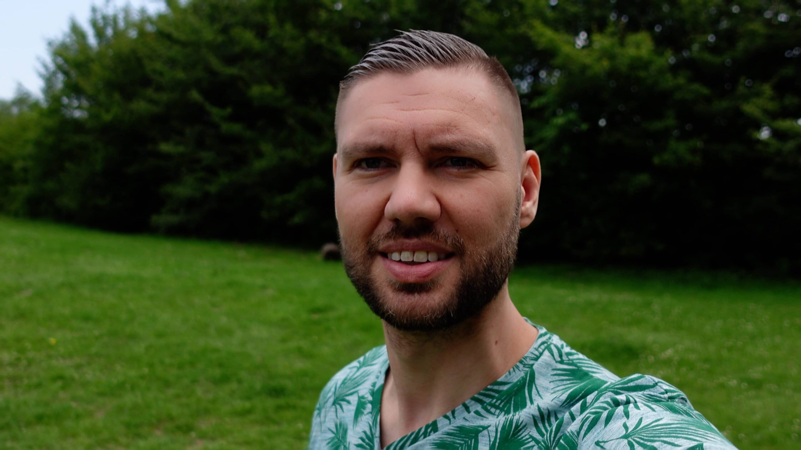 Portret van man in park met tropisch palmblad shirt en glimlach.