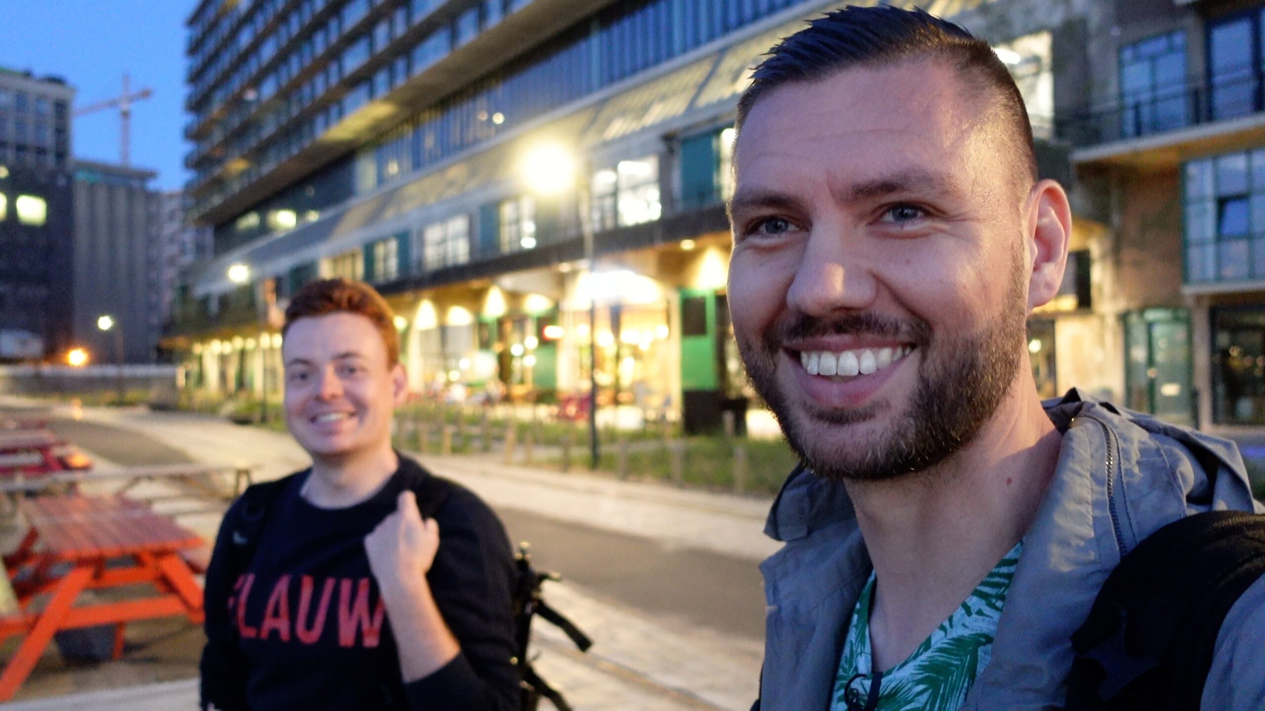 Selfie met twee vrienden tijdens blauwe uur op natte stadsstraat met buitenzitjes.