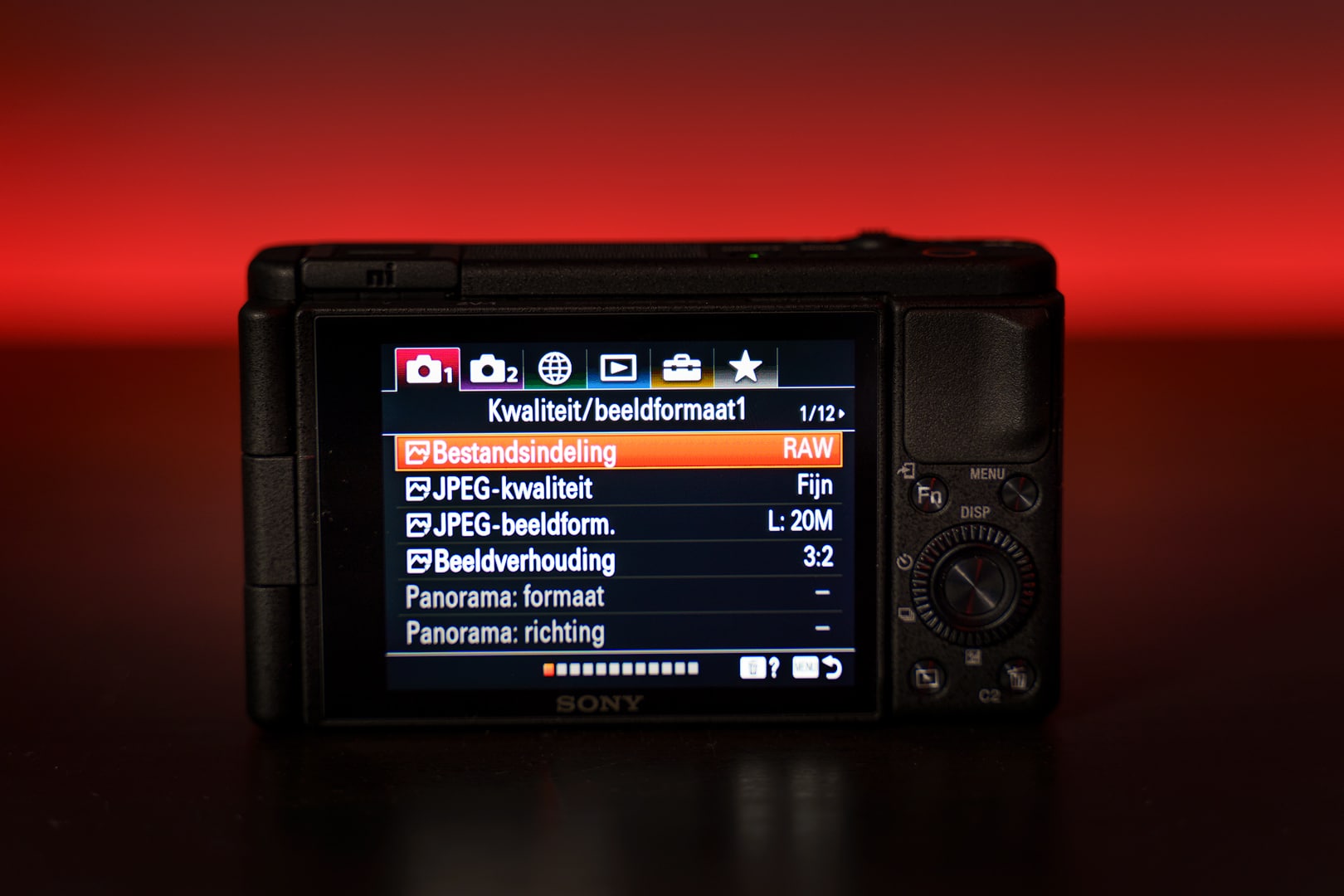 Sony ZV-1 achterkant met LCD-scherm en Nederlands menu, Bestandsindeling RAW en 3:2, rode achtergrond.