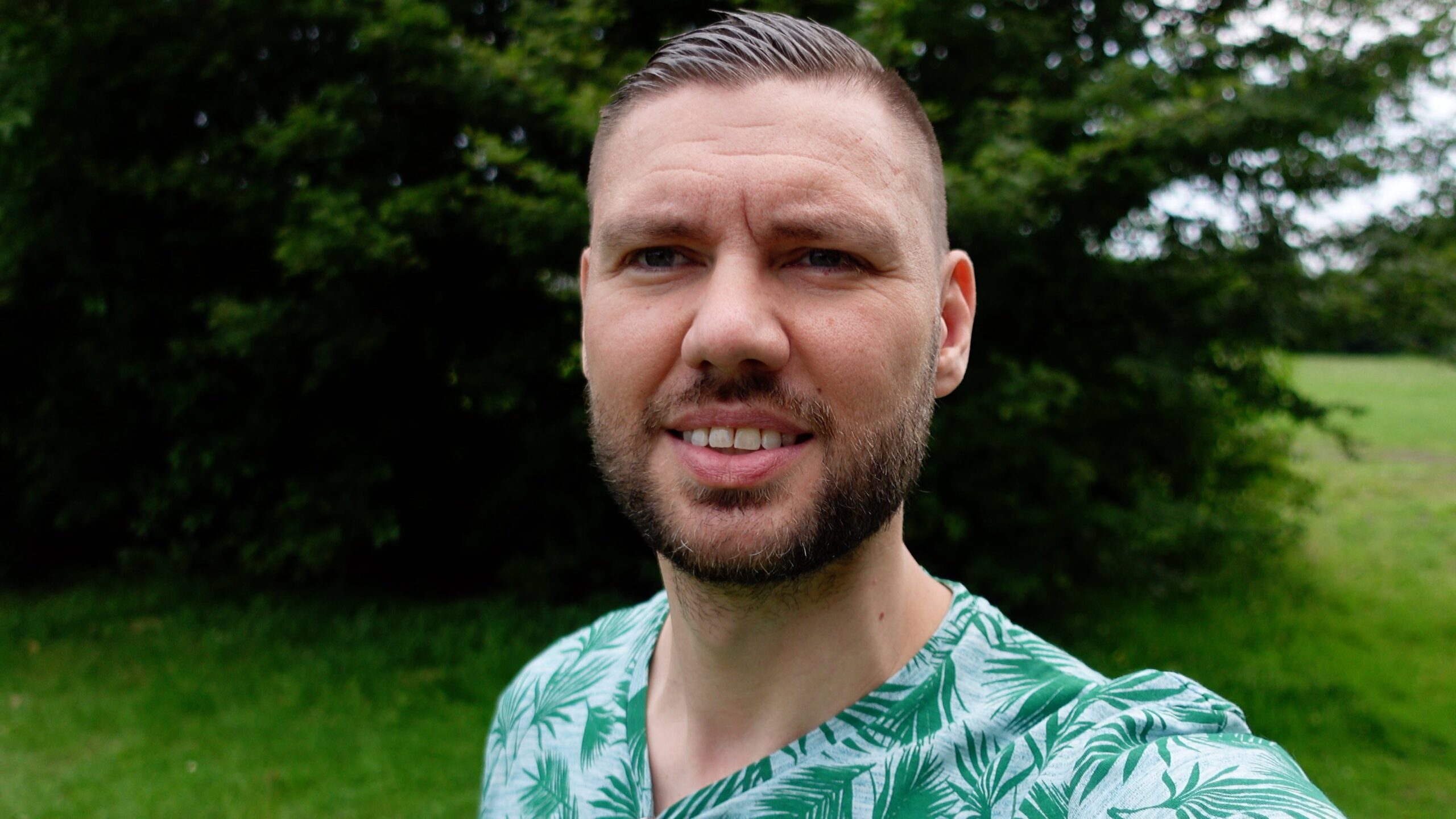 Zonnig portret van man in groen tropisch bladpatroon shirt tegen groene achtergrond.
