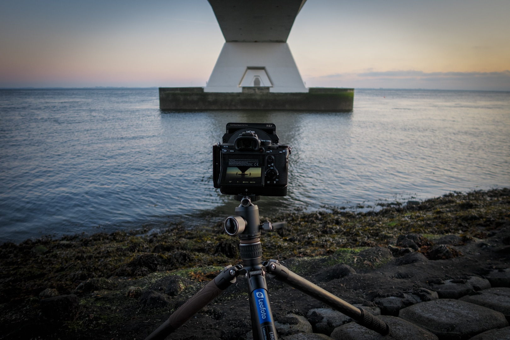 Fotograaf met tripod legt Zeelandbrug vast bij zonsondergang boven kalme zee
