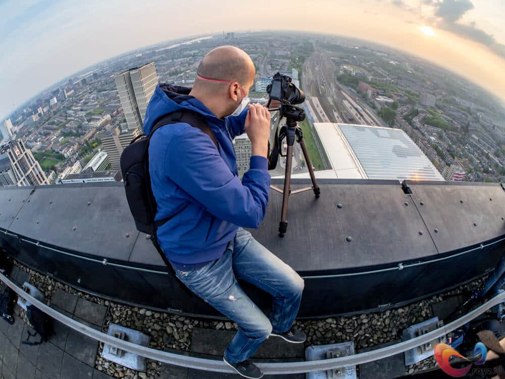 Fotograaf op dak bij zonsondergang legt stadsuitzicht vast met camera en statief.