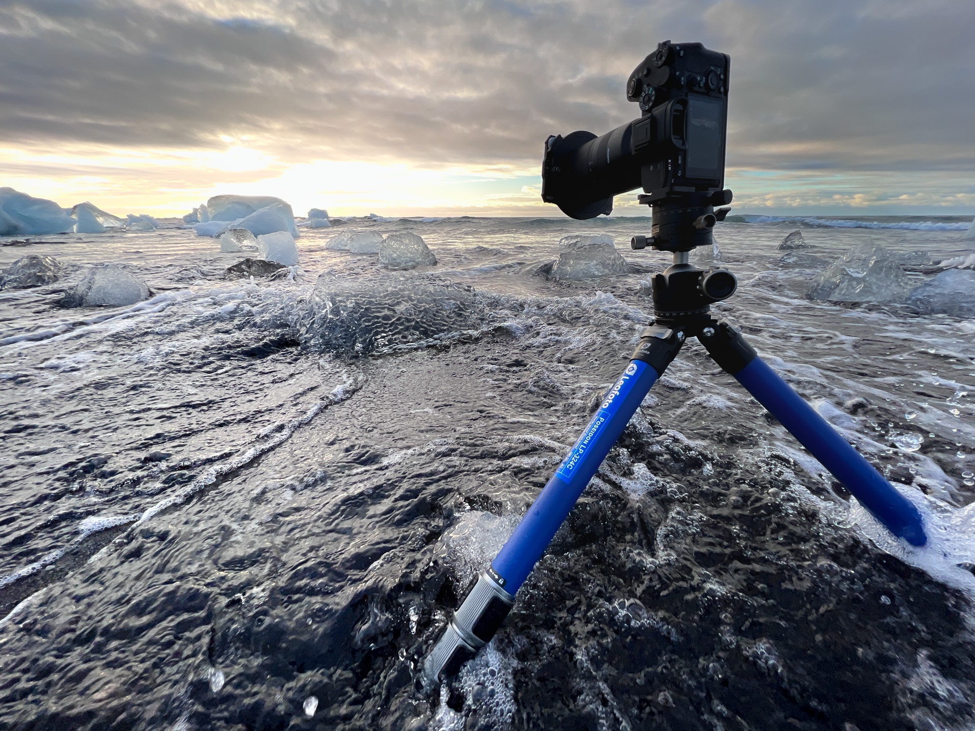 Blauw statief en camera aan polaire kust bij ijsblokken en oceaan in schemerlicht.