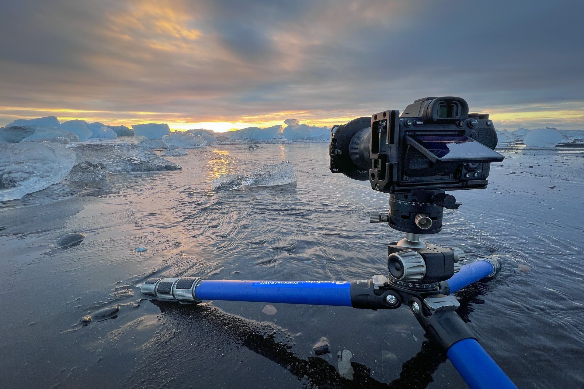 Camera op felblauw statief bij bevroren zee en zonsondergang met ijs.