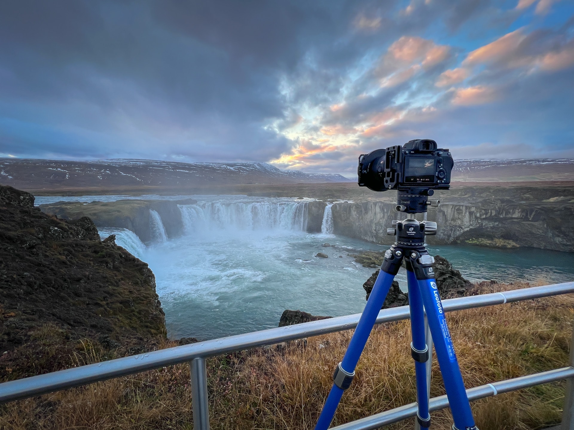 DSLR op Leofoto-statief bij een waterval met turkoois water en dramatische lucht.