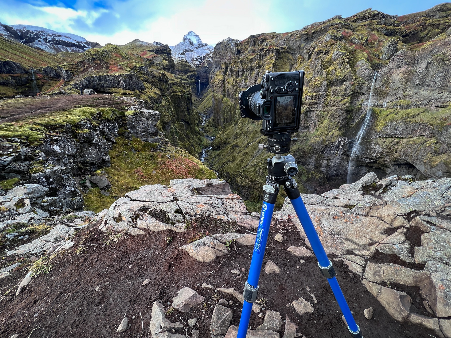 Grand Canyon landschap met camera op felblauw statief, waterval rechts, mosgroene wanden en rotsen.