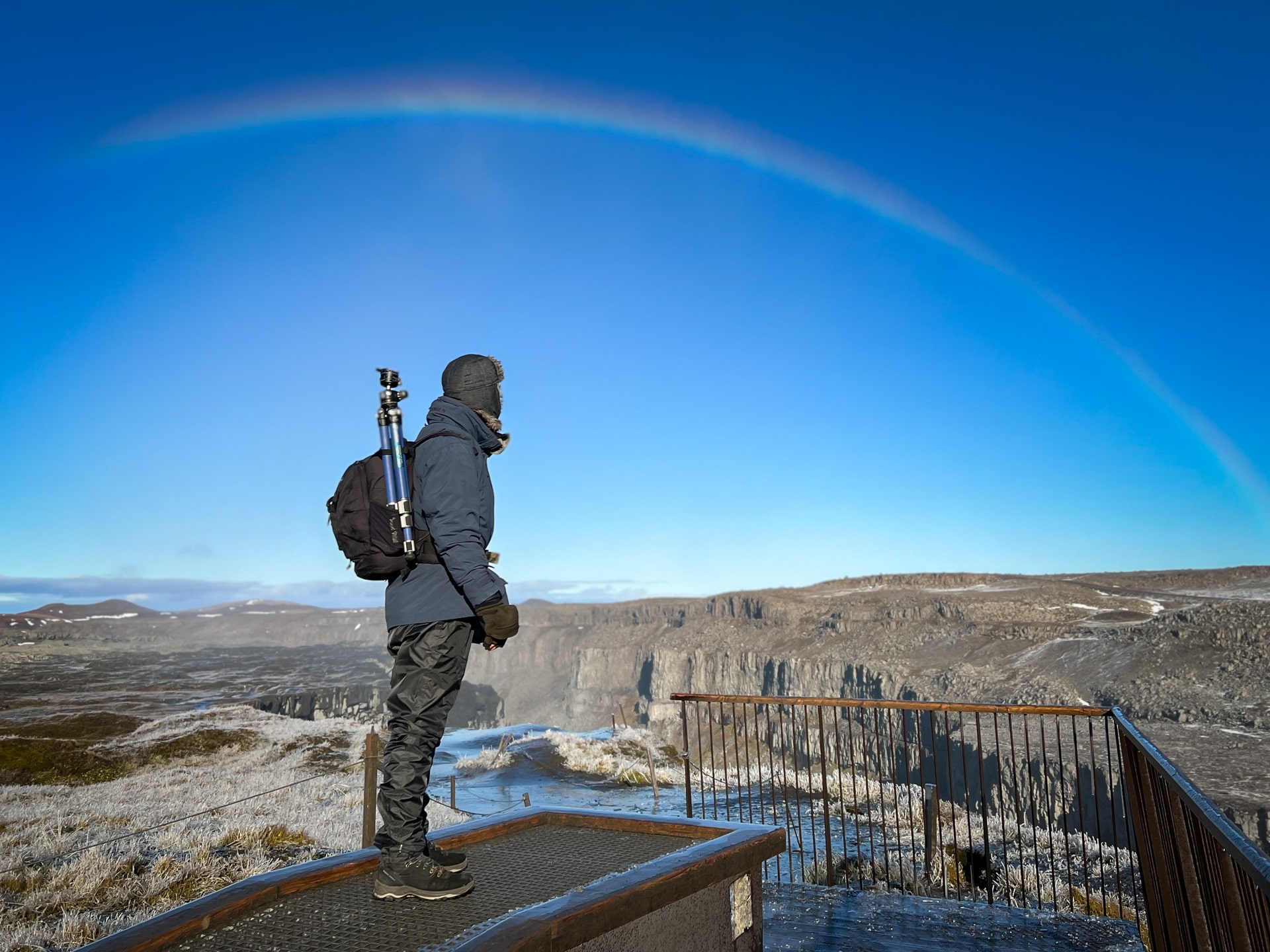 Fotograaf op bevroren observatieplatform met kliffen en halo in blauwe lucht.