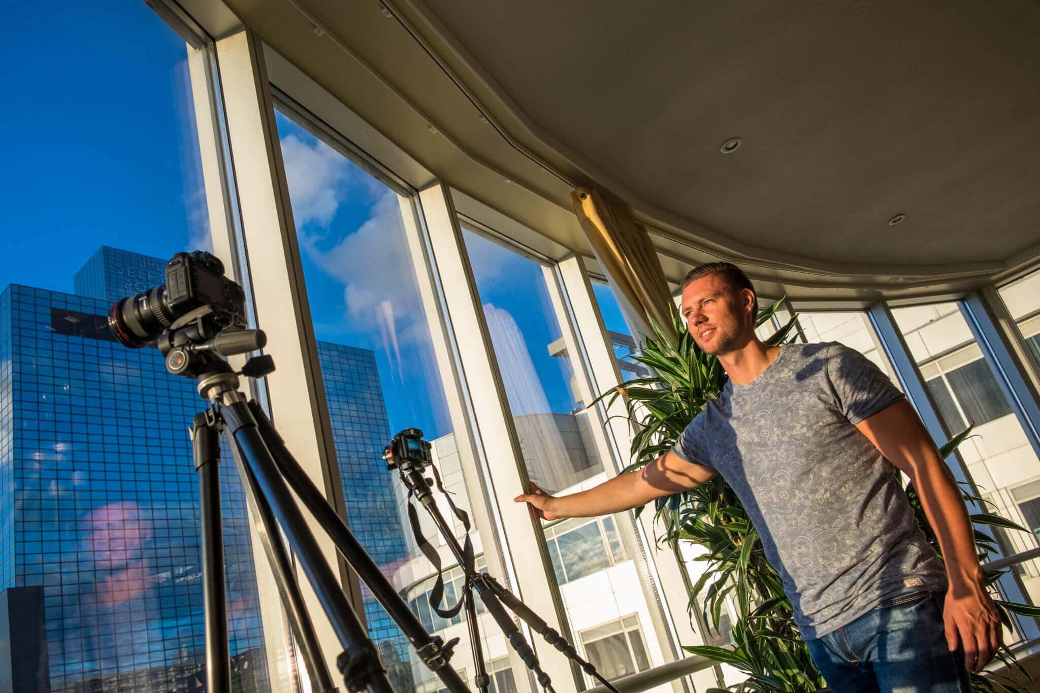 Man bij gebogen glazen kamer met twee cameras op statieven, uitzicht op wolkenkrabbers.