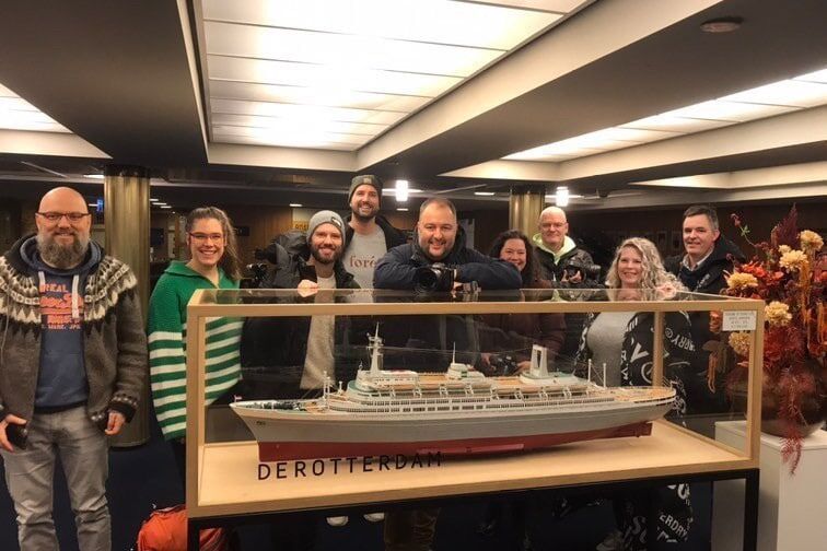 Diverse groep collega&rsquo;s poseert voor vitrinekast met SS Rotterdam scheepsmodel in museum.