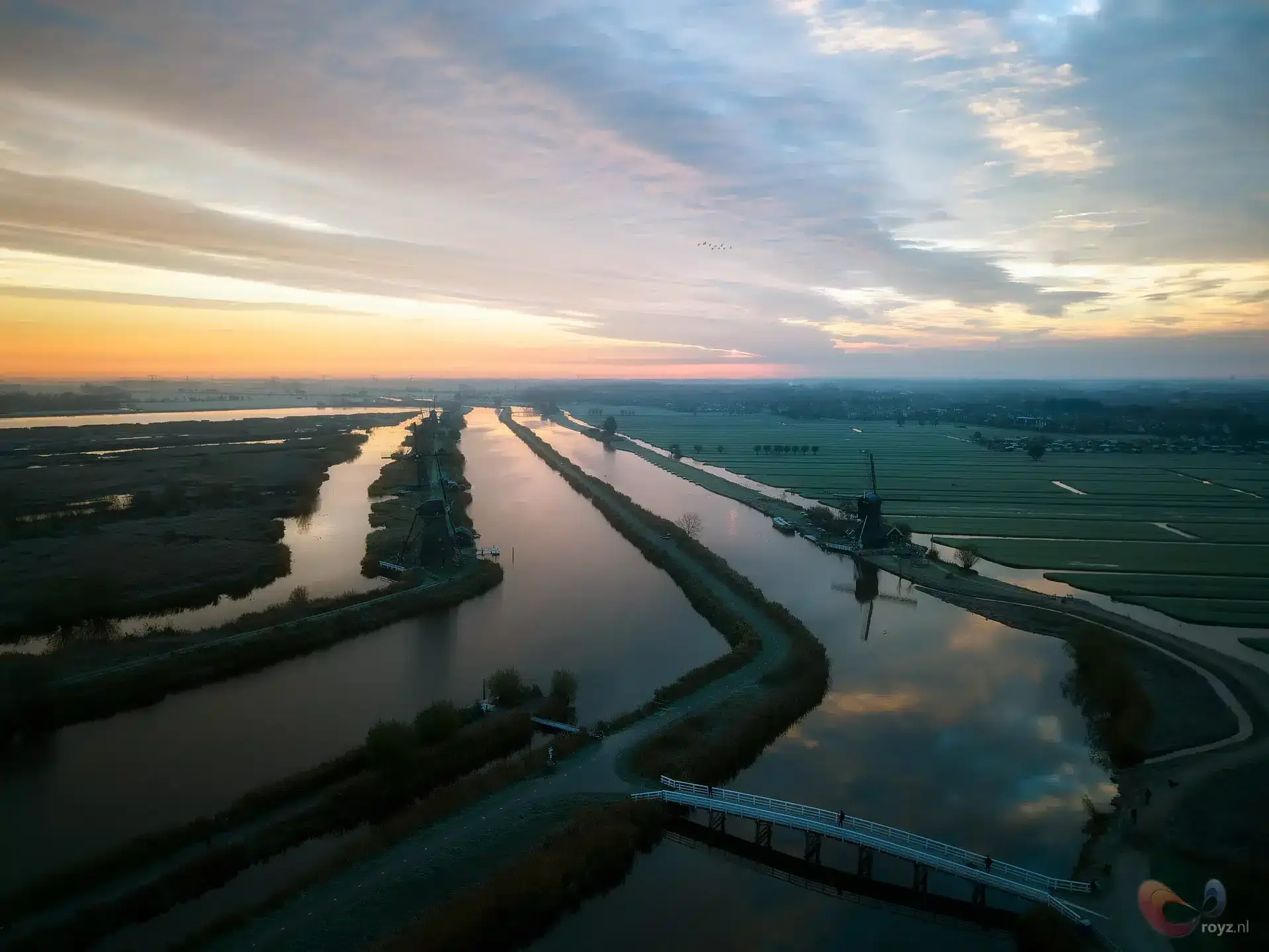 Zonsondergang bij Kinderdijk: windmolens langs kalme kanalen met reflecties en een brugsilhouet