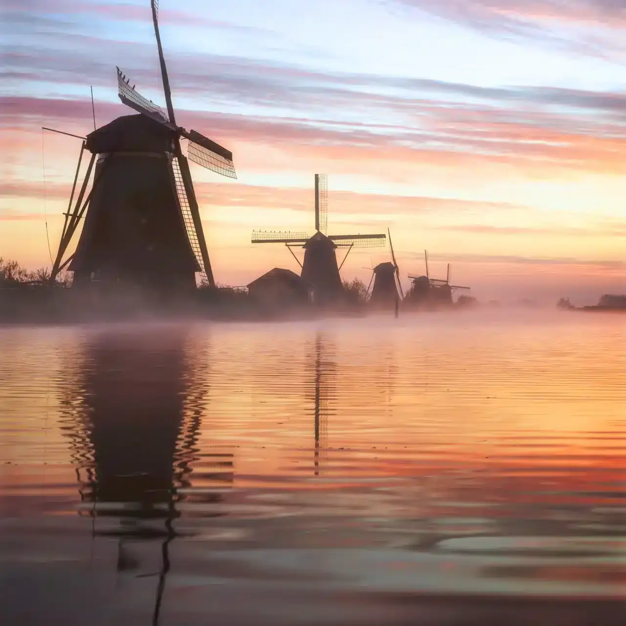 Dageraad bij Nederlandse windmolens: mist, water en reflecties.