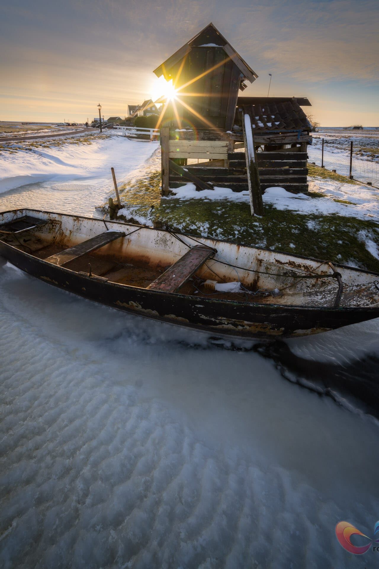 Bevroren kanaal, roestige roeiboot, scheef eilandhut; zonsondergang kleurt verlaten winterlandschap.