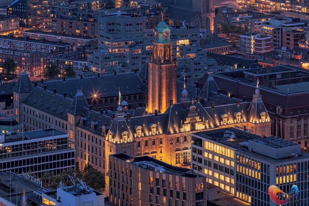 Blauwe uur: klokkentoren en historisch gebouw in een stadsgezicht met moderne glasarchitectuur en warm licht.