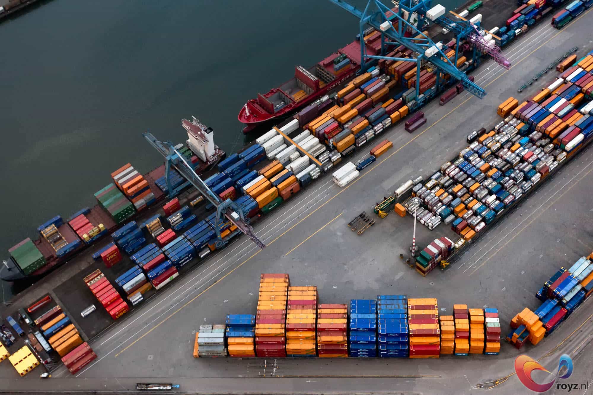 Luchtfoto van de Rotterdamse haven: blauwe kranen, rode vrachtschip en kleurrijke containers.