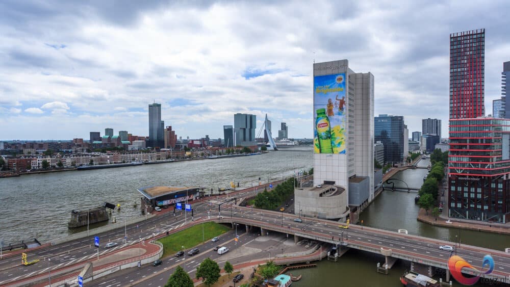 Rotterdam aan de rivier met Erasmusbrug, moderne skyline, viaducten en wit reclamegebouw met rode toren.