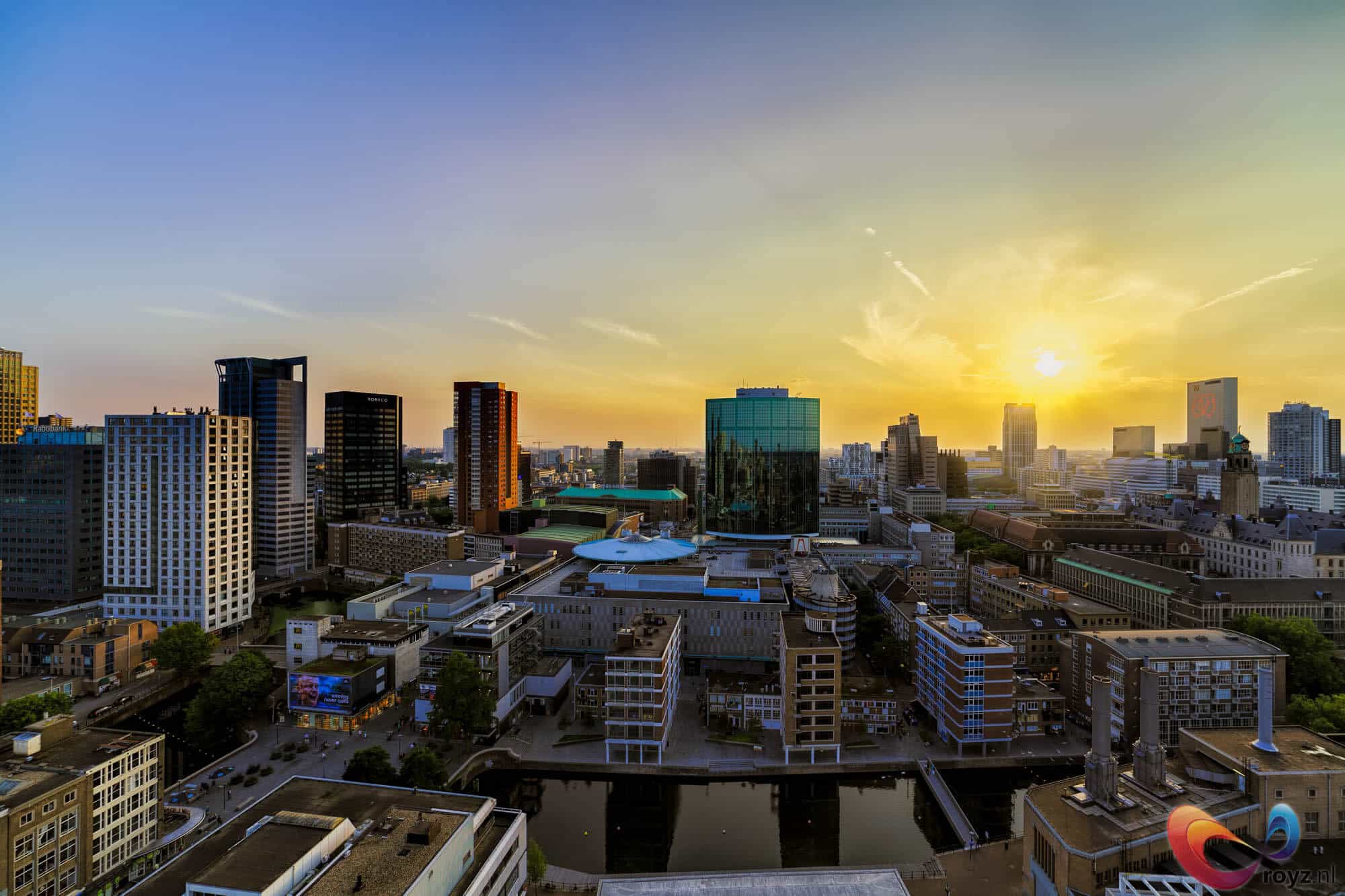 Rotterdam turquoise glazen toren bij zonsondergang met kanaal en wit rond dakgebouw