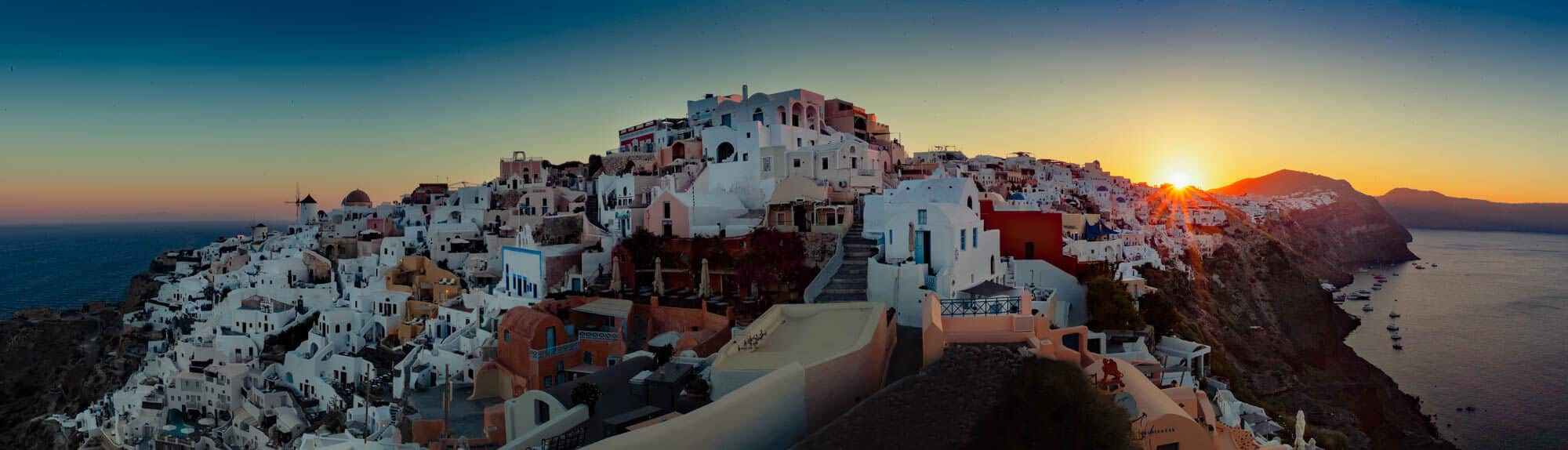 Santorini caldera dorp met witte huizen, blauwe koepels en zonsondergang boven de zee