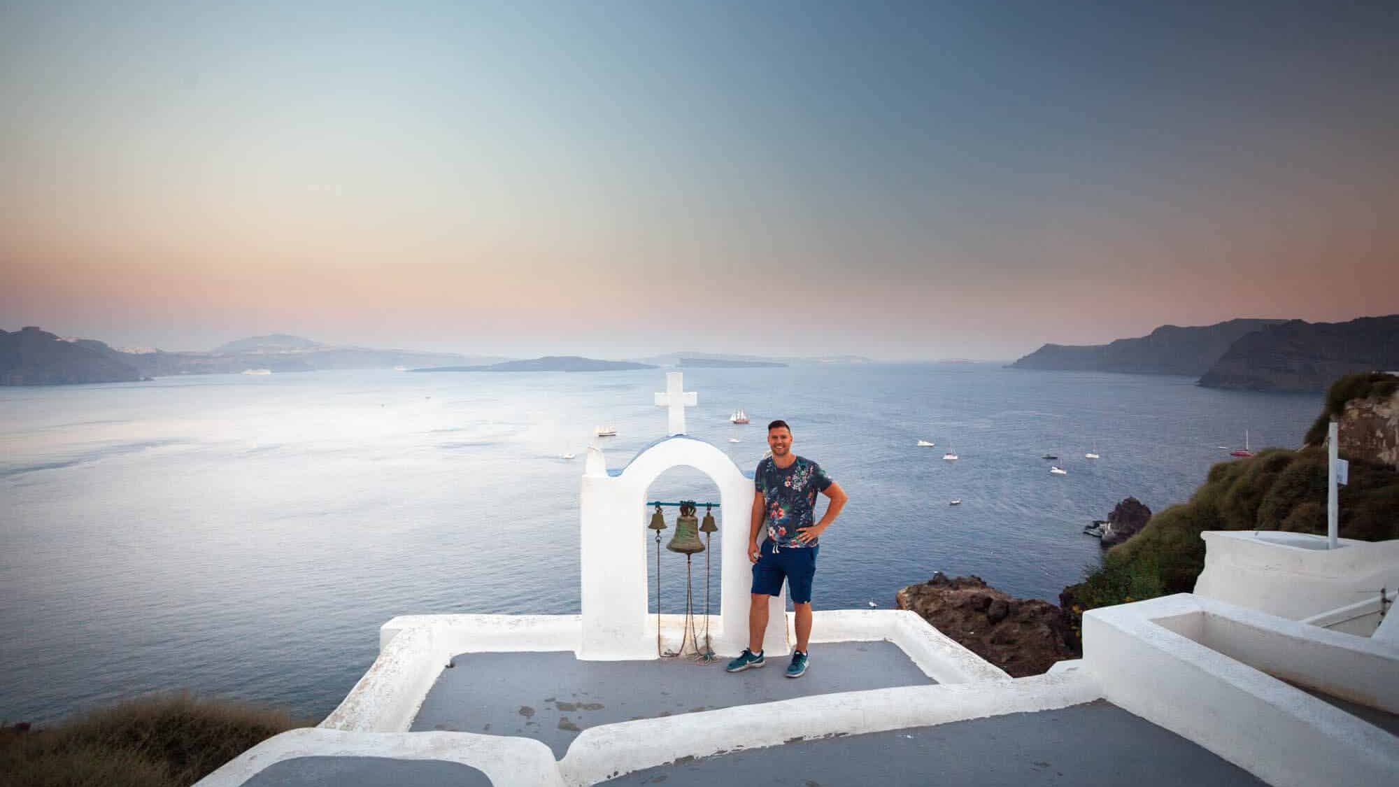 Santorini nis met twee bellen op wit terras aan zee bij zonsondergang.
