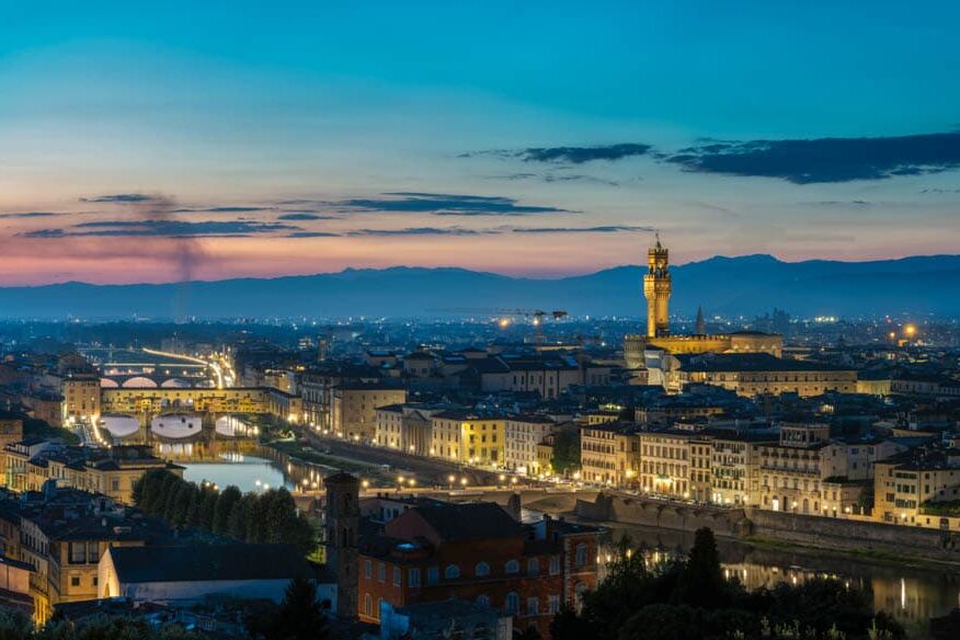 Florence bij schemer aan de Arno: Duomo en Palazzo Vecchio verlicht, amberkleurige daken.