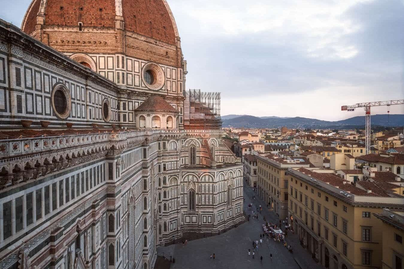 Duomo van Firenze vanaf Piazza del Duomo bij zonsondergang; koepel, marmeren gevel, gele gebouwen.
