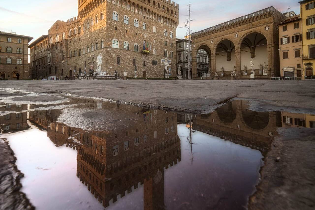 Palazzo Vecchio bij zonsondergang in Florence; plas weerspiegelt loggia met bogen en standbeelden