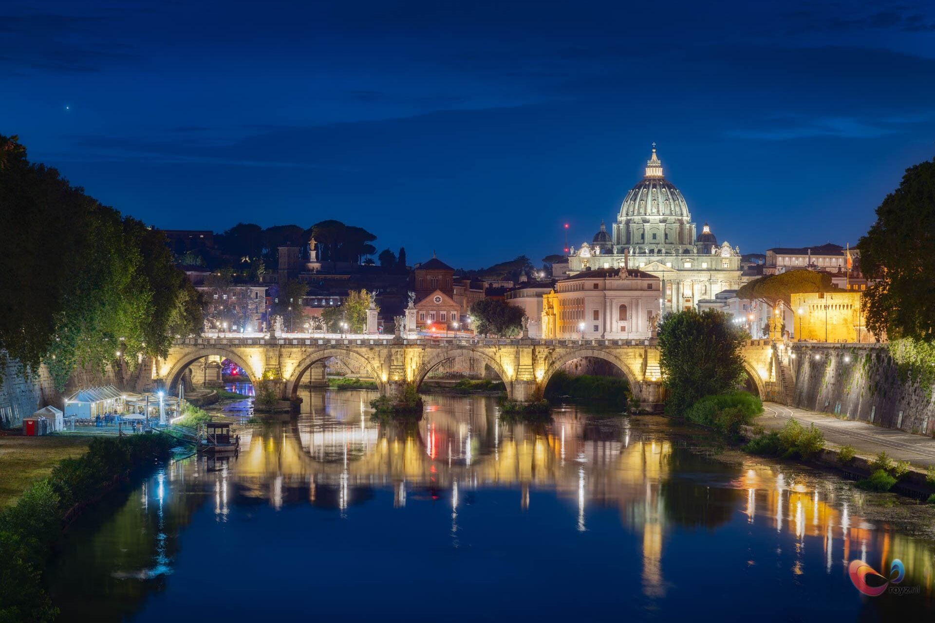 Nacht in Rome bij Sint-Pietersbasiliek: Tiber, koepel, en verlichte brug met reflecties.