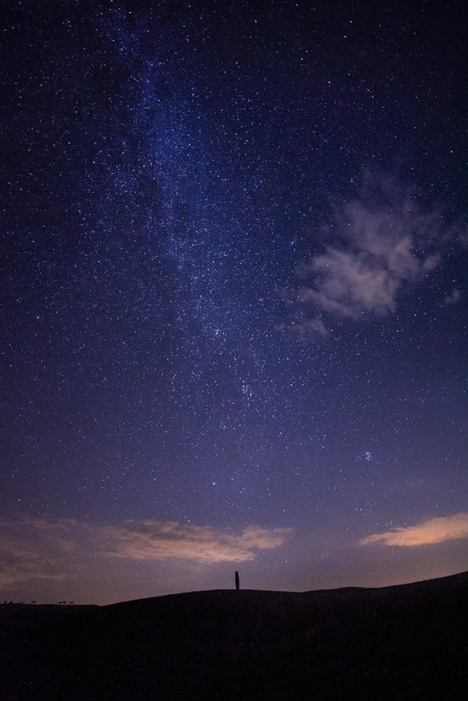 Eenzaam silhouet onder een sterrenrijke Melkweg boven rustige horizon.