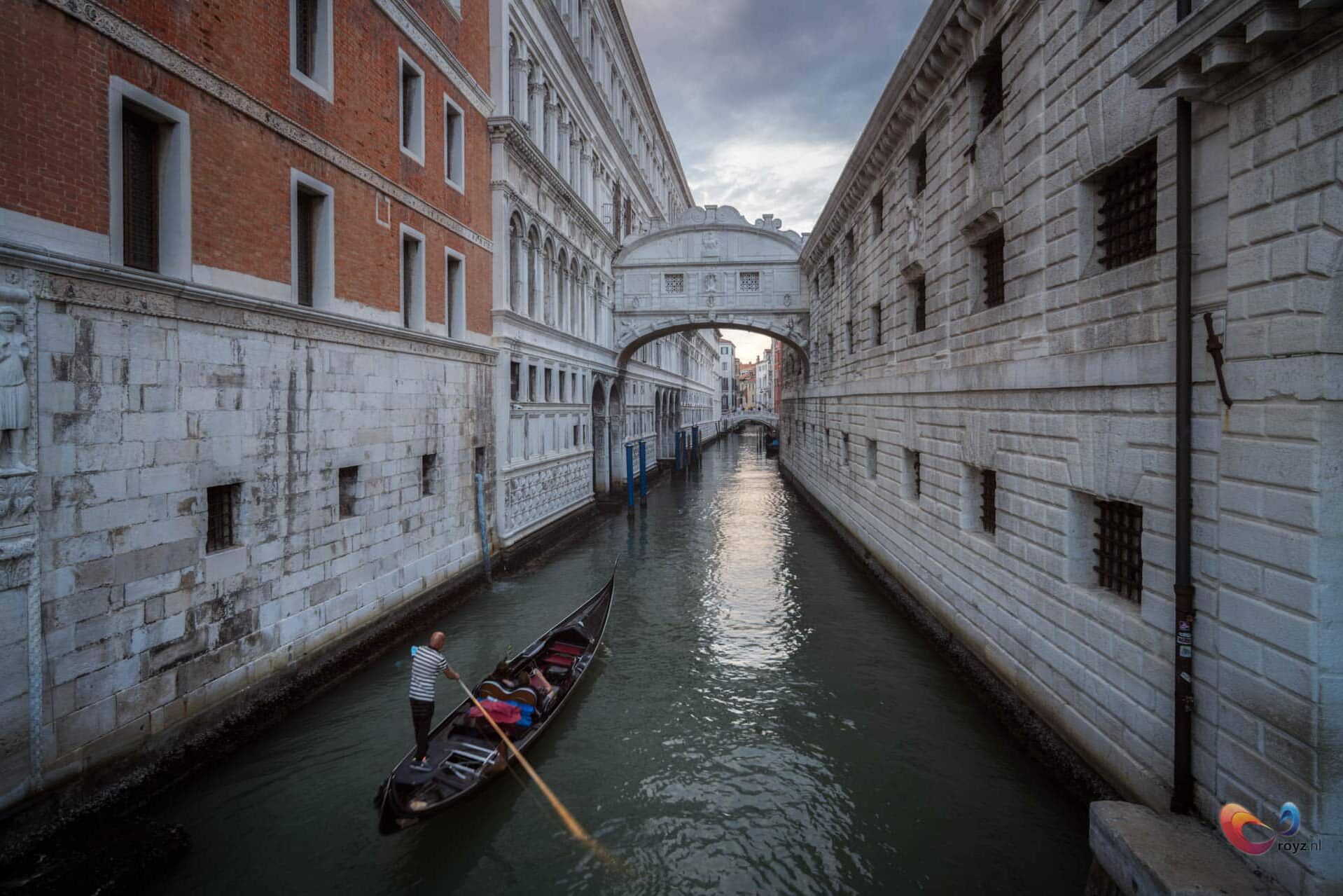 Gondola vaart door Venetië: kanaal onder marmeren brug tussen rode bakstenen gevels.