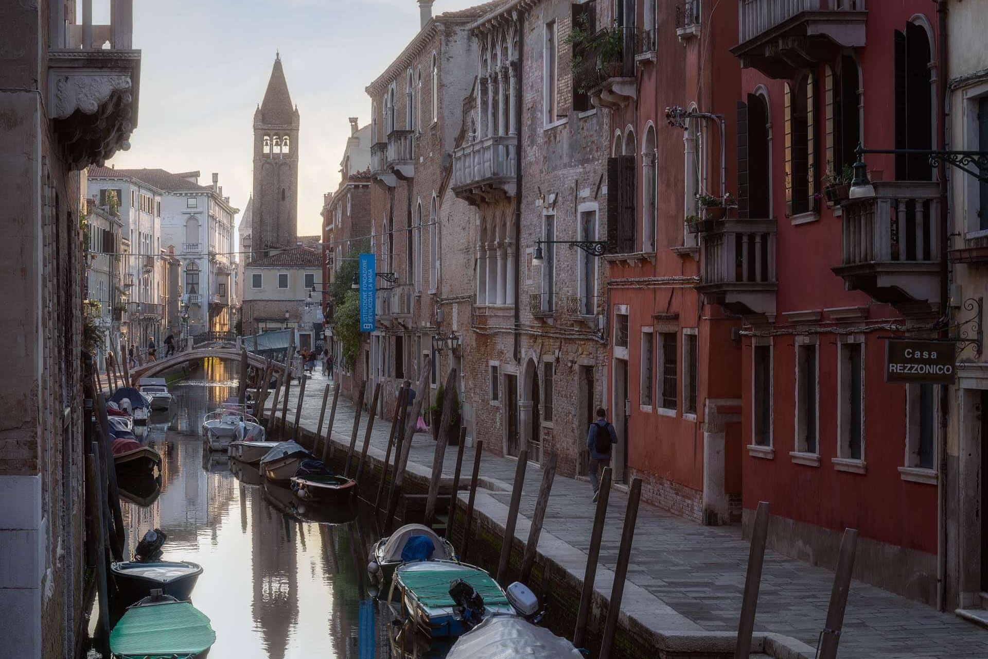 Italiaanse kanaalstad bij zonsondergang met oude huizen, boten en klokkentoren.