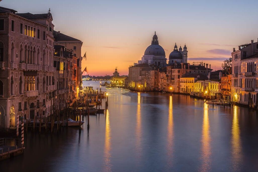 Venetië bij zonsondergang: kanalen, gotische palazzi, pastel gevels, gondolas en verlichte koepelkerk.