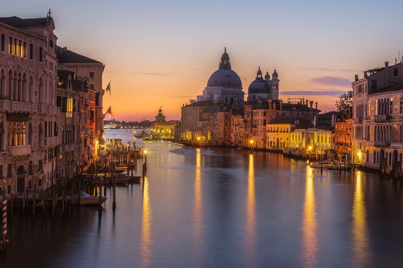 Venetië bij schemering langs het Grand Canal: palazzi, lampen en een koepelkerk op de achtergrond.
