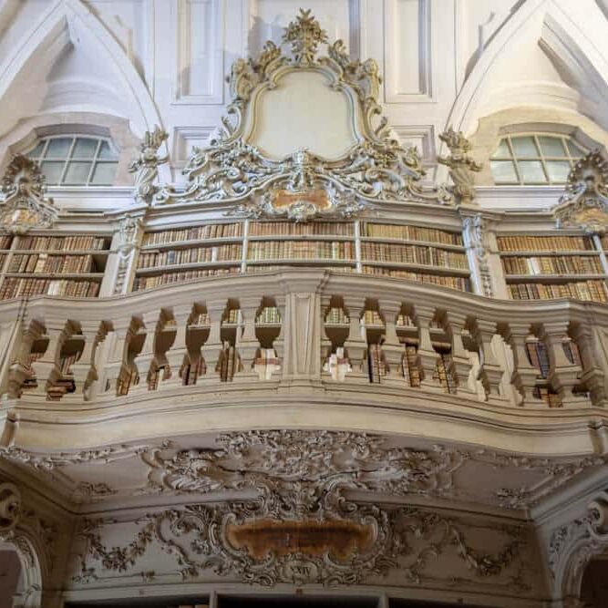 Weelderige bibliotheek met balkon, witte pleister, gouden rococo en leren boekenkasten.